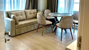 A modern living room with a beige sofa, two armchairs, a round coffee table, and a dining table with chairs. - Modern Seaside Retreat · Stunning Sea View (Constanța)