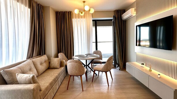 A modern living room with a sofa, chairs, a dining table, and a flat-screen TV mounted on the wall. - Modern Seaside Retreat · Stunning Sea View (Constanța)