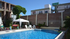 Ein Pool mit weißen Stühlen und einem weißen Zelt, umgeben von Backsteingebäuden und Grünflächen.