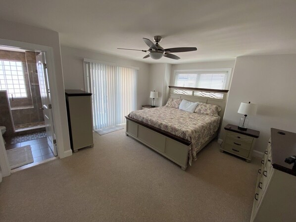 A bedroom with a bed, a nightstand, a dresser, a ceiling fan, and a door leading to a bathroom.