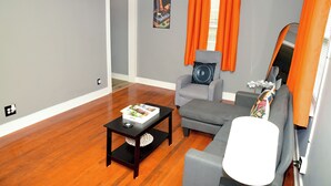 A modern living room with hardwood flooring, a gray sofa, a white ottoman, and a black coffee table.