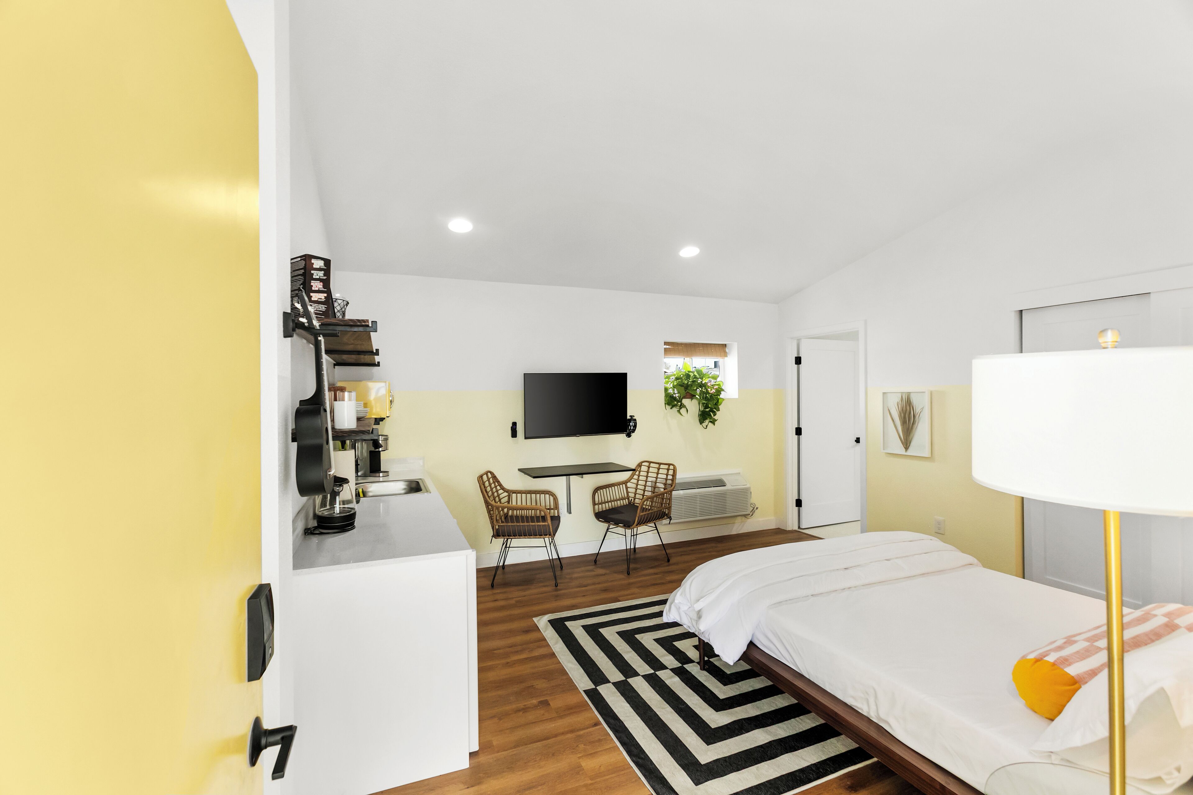 Une chambre d’hôtel moderne équipée d’un lit, d’un bureau, de deux chaises, d’une télévision et d’une plante.