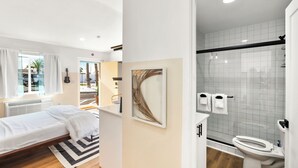 A modern bedroom with a bed, a window with curtains, a guitar, and a framed artwork on the wall.
