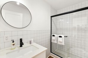 A bathroom with a white sink, a black faucet, a round mirror, and a glass shower enclosure.