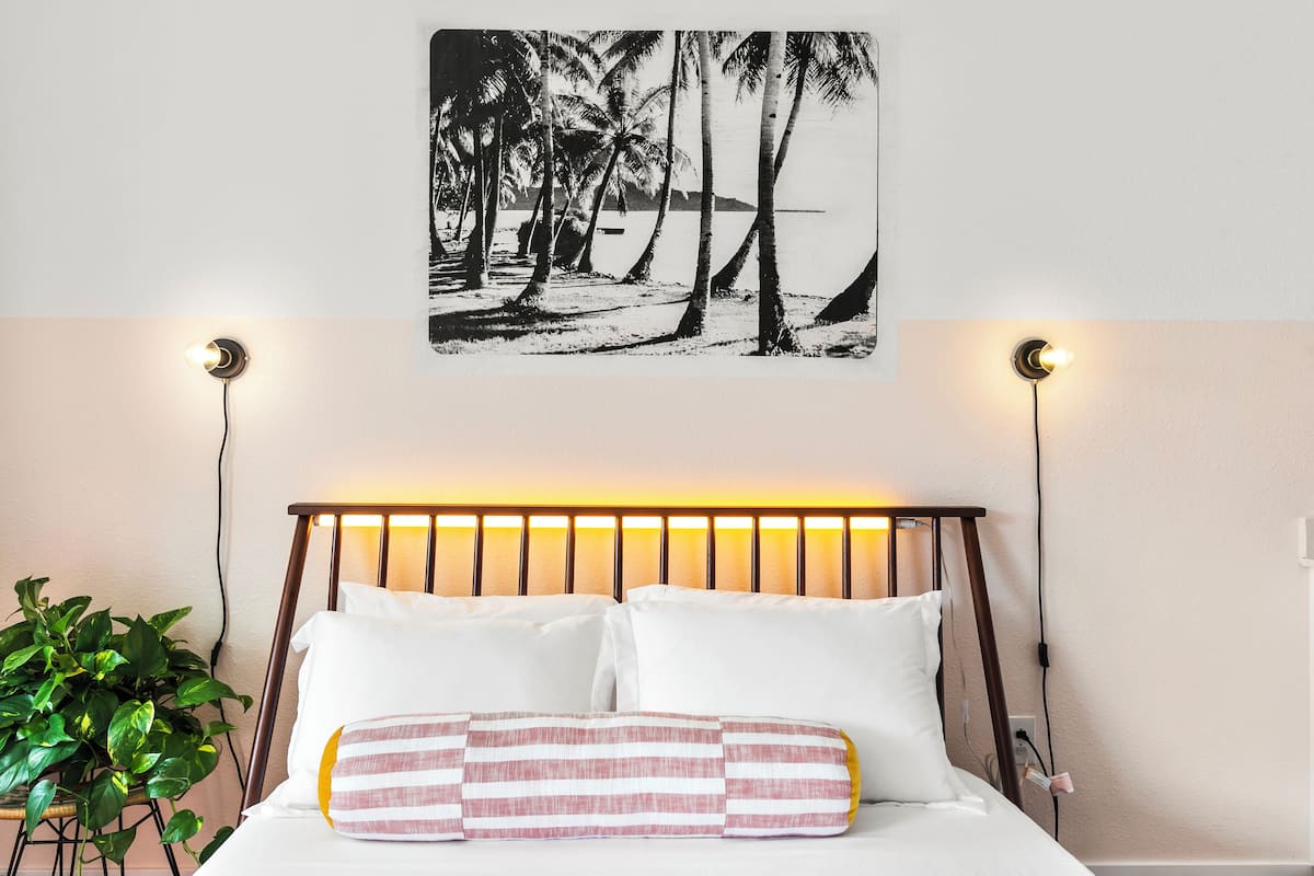 A bedroom with a bed, a wall-mounted picture of a beach, and bedside lamps.