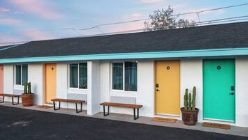 Un motel con puertas numeradas, bancos y cactus en macetas.