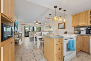 A kitchen with wooden cabinets, a dining area with a table and chairs, a ceiling fan, and pendant lights.