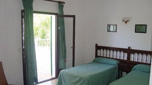 A room with two single beds, a wooden headboard, a chair, and a sliding glass door leading to an outdoor area. - Oasis D Or (Santanyi)
