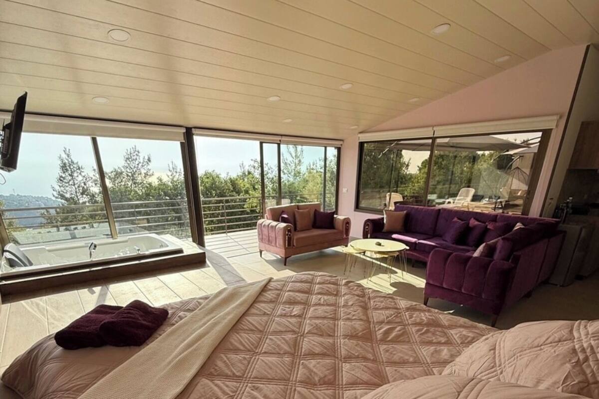 A modern bedroom with a large bed, two sofas, and a balcony with a view.