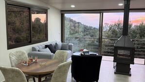 A modern living room with a dining area, large windows, and a wood-burning stove. - Amaruna Lb - Aroma (Ghadras)