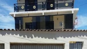 A building with a flat roof, a balcony on the upper floor, and three large, closed garage doors. - Pousada Vila Piatã (Salvador)