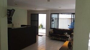 A spacious living area with a large window, a sofa, and a television. - Pousada Vila Piatã (Salvador)