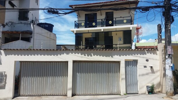 A building with three large garage doors, a balcony with a TV and WiFi sign, and a visible address number 49. - Pousada Vila Piatã (Salvador)