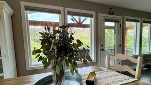 A dining area with a wooden table, a vase with green foliage, and a candle. - Stillwater River Front Montana Home (Nye)