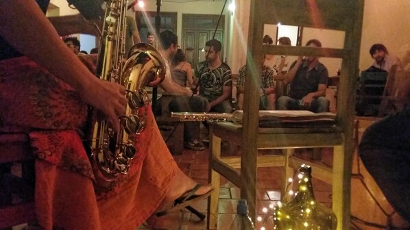 A room with a person playing a saxophone, a table with a bottle, and a mirror reflecting the room. - Esperanto Hostel (Salta)