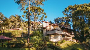 A two-story house with a balcony, surrounded by trees and a fenced garden. - Village 31 (Campos do Jordão)