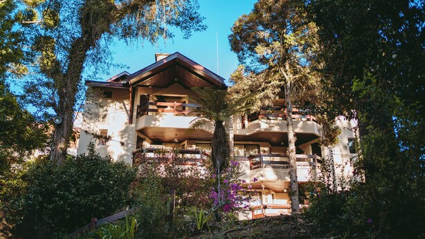 A multi-story building with balconies, surrounded by trees and vegetation. - Village 31 (Campos do Jordão)