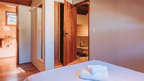 A hotel room with a wooden floor, a bed with white linens, a bathroom with a sink and mirror, and a view through an open door. - Village 31 (Campos do Jordão)