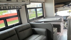 Un interno camper moderno con un divano in pelle grigio, un tavolo da pranzo e un angolo cottura.