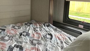 Interni di un camper compatto con un letto, una finestra con il cartello 'EXIT' e vista su un prato.