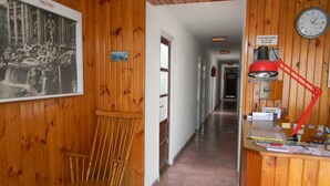 Ein hölzerner Korridor mit Holzvertäfelung, einem Holzstuhl, einem gerahmten Bild, einer Uhr und einem Schreibtisch mit einer roten Lampe.