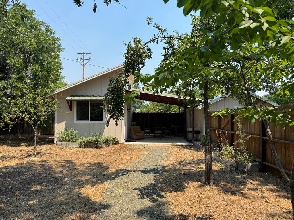 A single-story house with a covered porch, a fenced backyard, and a gravel driveway.