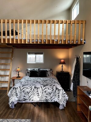 A loft bedroom with a bunk bed, a bedside table with a lamp, a TV, and a window with a view. - The Well House with outdoor seating and loft! (Middletown)
