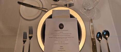 Une table à manger dressée de façon élégante, avec un menu, des couverts et des bougies.