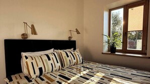 A bedroom with a bed, a window with a plant, and two wall-mounted lamps. - Brand New Apt in Historic Cesis (Cēsis)