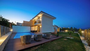 Ein modernes Haus mit Swimmingpool, Sitzgelegenheiten im Freien und einem gepflegten Garten.