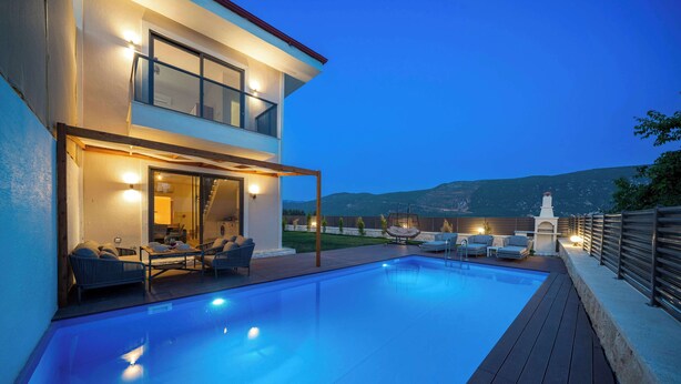 Ein modernes, zweistöckiges Haus mit Swimmingpool, Sitzgelegenheiten im Freien und Bergblick.