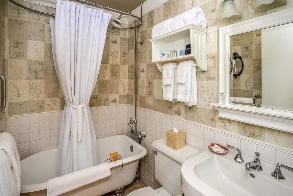 Casa de banho com banheira, lavatório e chuveiro. Toalhas e artigos de higiene pessoal estão nas prateleiras.
