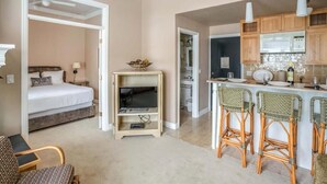 Ein kompaktes Hotelzimmer mit Bett, Fernseher, einer kleinen Küchenzeile und einer Essecke mit Barhocker.