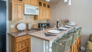 A kitchen with wooden cabinets, a microwave, a sink, and a bar area with chairs. - Pet-Friendly Suite Near Cannon Beach – Quick Access! (Cannon Beach)