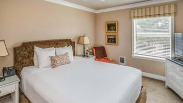 Une chambre d’hôtel avec un grand lit, une table de chevet avec une lampe, une chaise, un téléviseur et une fenêtre avec des stores.