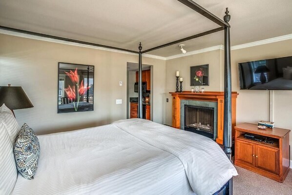 Un lit à baldaquin avec une couvre-lit blanche, une cheminée avec un manteau de cheminée et un téléviseur fixé au mur.