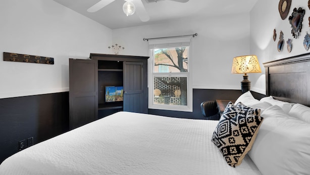 Un dormitorio con cama, ventilador de techo, ventana y lámpara de pared.