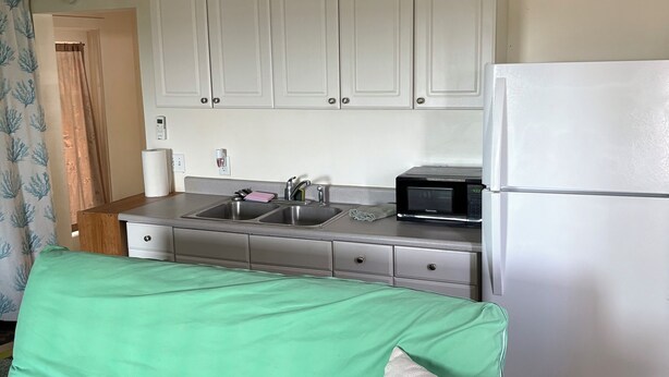A compact kitchen with white cabinets, a stainless steel sink, a microwave, and a white refrigerator.