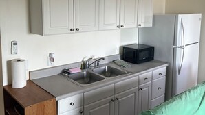 A kitchen with white cabinets, a stainless steel sink, a black microwave, and a white refrigerator. - Cozy studio in awesome Kaaawa with WiFi, AC, fitness room (Kaaawa)
