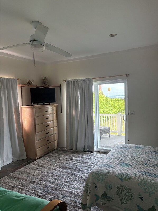 A bedroom with a bed, a dresser, a ceiling fan, and a sliding glass door leading to a balcony.