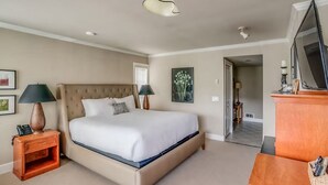Une chambre à coucher avec un grand lit, deux tables de chevet avec des lampes, une commode en bois et un téléviseur.