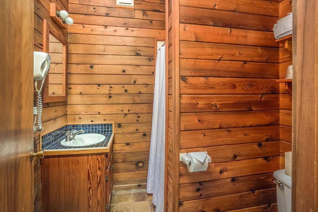 Une salle de bain rustique, avec des murs en bois, comprenant un lavabo, un miroir et un porte-serviettes.