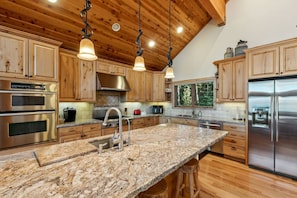 Una cocina con armarios de madera, electrodomésticos de acero inoxidable, encimeras de granito e iluminación colgante.