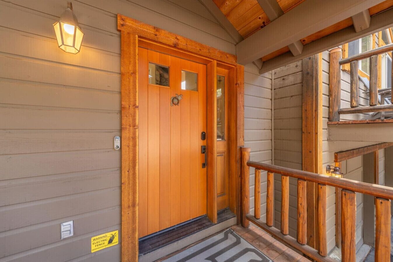 A wooden door with a glass panel, a wooden railing, and a warning sign for electric fence.