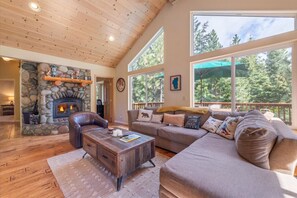 Un salón acogedor con chimenea de piedra, techo de madera, ventanas amplias y un sofá cómodo.