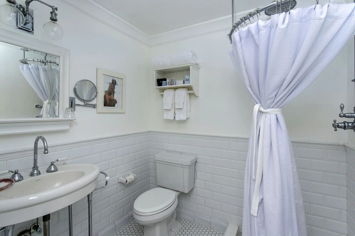 A bathroom with a white sink, toilet, and shower curtain. There is a towel rack with towels and a framed picture on the wall.