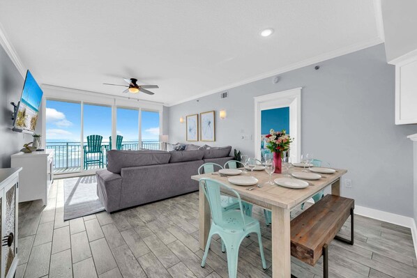 A modern living room with a gray sofa, teal chairs, and a wooden dining table set for four.