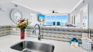 A modern kitchen with a large sink, a decorative mirror, and a view of the ocean through large windows.