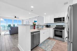 A modern kitchen with stainless steel appliances, a dishwasher, and a view to the outside. - 🦩Book Me Baby! Gulf-Front Waterscape B401 Sundrenched🦩 (Fort Walton Beach)