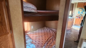 A compact RV bedroom with a bunk bed, wooden cabinetry, and a small kitchenette. - Unique getaway or travel stop, just 10 minutes off TransCan Highway (Grand Sudbury)